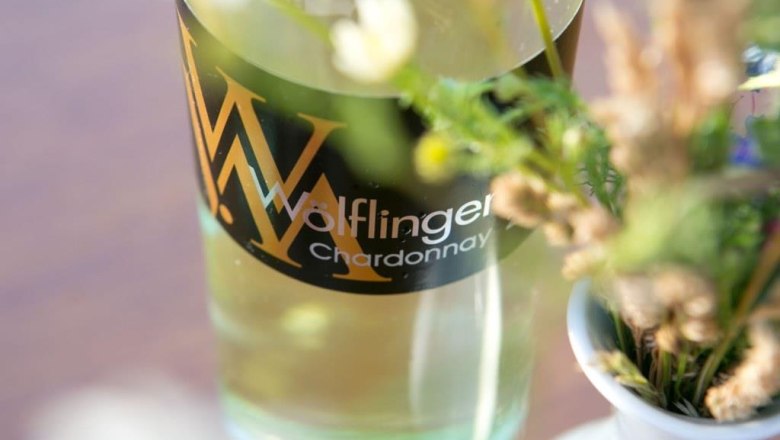 Weinbau Wölflinger, © Fotohaus Hans Krist Nahaufnahme einer Weinflasche mit der Aufschrift 'Wölflinger Chardonnay' neben einem Blumenstrauß.