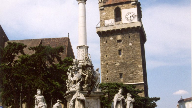 Wehrturm, © Perchtoldsdorf Historischer Wehrturm mit Uhr und barocker Säule im Vordergrund.
