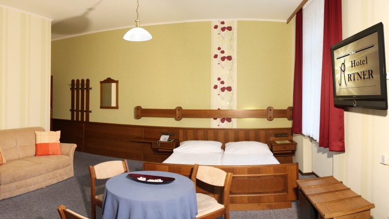 Zweitbettzimmer, © Schwertfuehrer Christian Hotelzimmer mit Doppelbett, Sofa, Tisch und Fernseher.