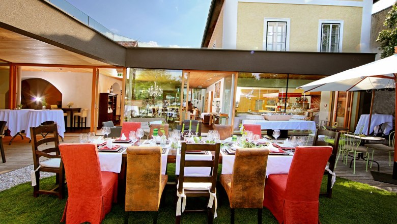 Blackboard, © Hotel Landhaus Moserhof GmbH Elegant restaurant with an outdoor table surrounded by modern buildings.