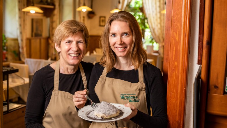 Edith und Tochter Elvira Smetana, © Niederösterreich Werbung/Kurt Pinter Zwei Frauen in Schürzen halten einen Teller mit einem Dessert in einem gemütlichen Restaurant.