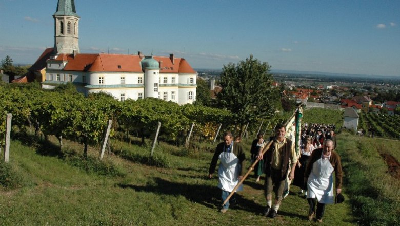 Municipality of Gumpoldskirchen, © Gemeinde Gumpoldskirchen People in traditional dress walk through vineyards in Gumpoldskirchen, with a church and buildings in the background.