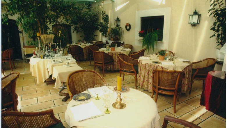 Landhotel Jagdhof Wintergarten, © Familie Fakler Ein gemütlicher Wintergarten eines Landhotels mit gedeckten Tischen, Pflanzen und Korbstühlen.