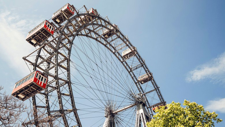 Wiener Riesenrad, © Wiener Riesenrad Das Wiener Riesenrad vor blauem Himmel mit grünen Bäumen im Vordergrund.