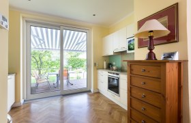 Kueche, © Creative Design Helle Küche mit Parkettboden, Schrank, Herd und großer Glastür zur Terrasse mit Markise.