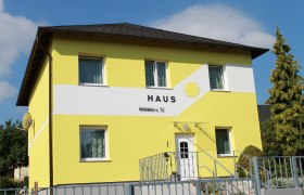Eingang Haus Sonne, © privat Gelbes Haus mit der Aufschrift 'Haus' und einer Sonne auf der Fassade.