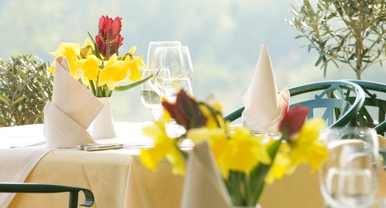 Gedeckter Tisch, © F. Bläuel GesmbH Ein elegant gedeckter Tisch im Freien mit gelben und roten Blumen, weißen Servietten und Weingläsern.