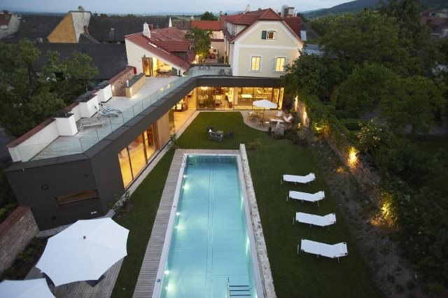 Außenbereich, © Hotel Landhaus Moserhof GmbH Luftaufnahme eines modernen Hauses mit Pool und Garten bei Abenddämmerung.