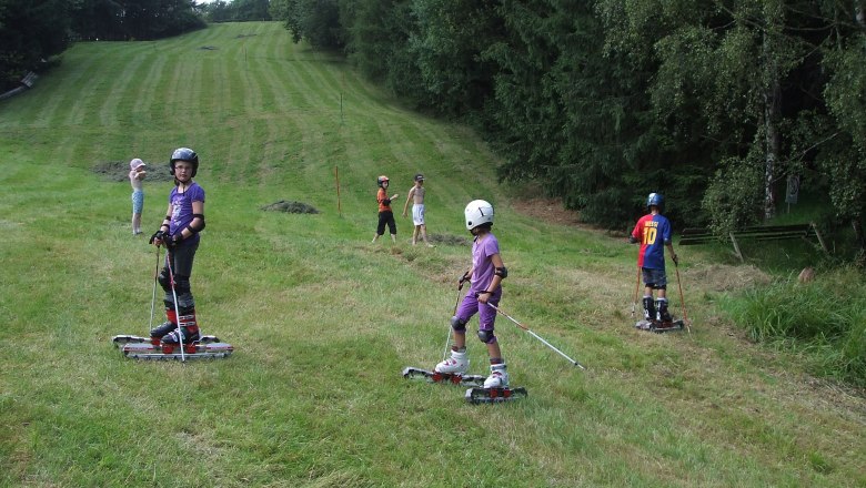 Skigebiet Oberkirchbach, © Bonka GmbH Kinder fahren mit Grasskiern auf einer Wiese.
