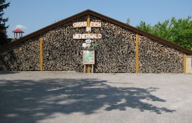 Aussenansicht, © Gasthof Skilitz Holzstapel mit Schild 'Griaß Eich im Wienerwald'.