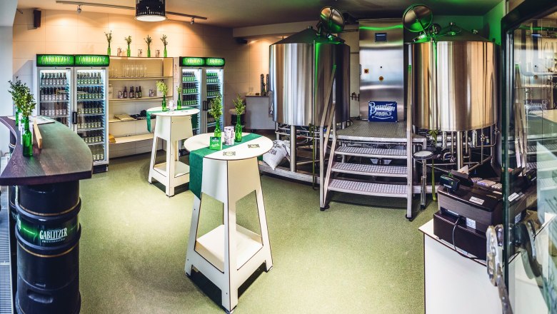 Shop und Sudhoff, © Mario Pampel Innenansicht einer kleinen Brauerei mit Edelstahlkesseln und Kühlschränken voller Getränke.