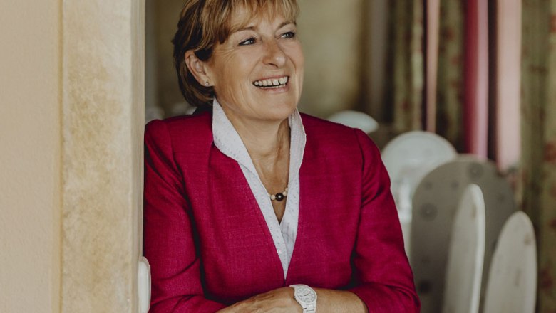 Schattiger grüner Gastgarten, © Niederösterreich Werbung/Sophie Menegaldo Frau in rotem Blazer lächelt und lehnt sich an eine Wand.