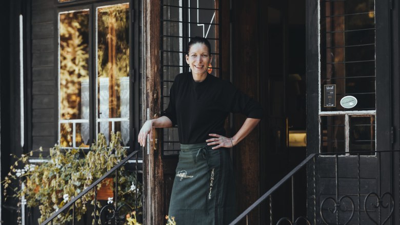 A warm welcome from landlady Brigitte Blanka, © Niederösterreich Werbung/David Schreiber A woman stands smiling in the doorway of a rustic building with plants in the foreground.