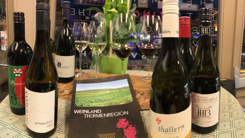 Enjoy in style, © Vino Neustadt Wine bottles and glasses on a table with a brochure of the Thermenregion wine region.