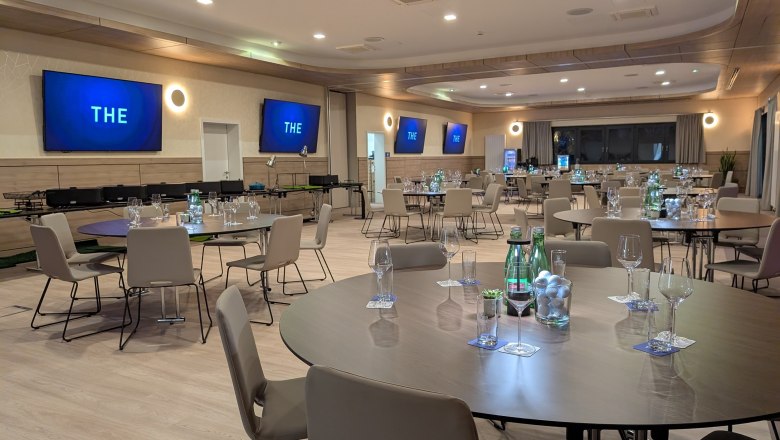 Topgolf Wien, Seminarraum, © Topgolf Wien Moderner Seminarraum mit runden Tischen, Stühlen und Bildschirmen an den Wänden.