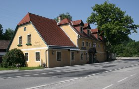 Gasthof Renzenhof, © zVg Gasthof Renzenhof Gelbes Gasthaus mit rotem Dach an einer Straße, umgeben von Bäumen.