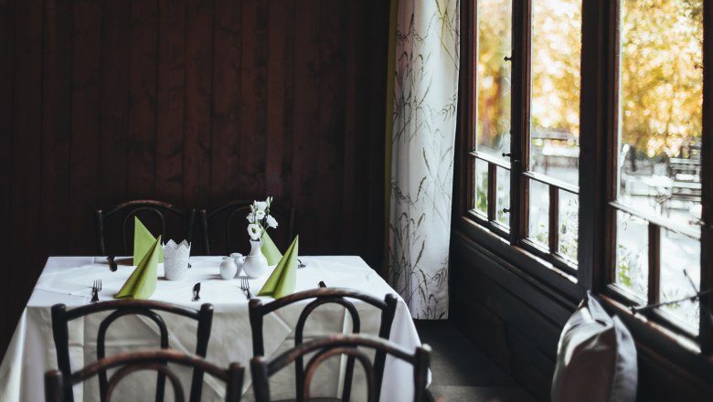 Restaurant with inventory from the 20s, © Niederösterreich Werbung/David Schreiber A table in an inn with wooden chairs, white tablecloths and green napkins, next to a window with curtains.