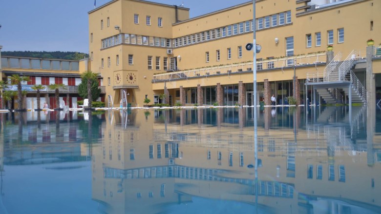 Outdoor pool, © Freizeitzentrum Stadtbad Mödling An outdoor pool with a large yellow building in the background, reflected in the water.