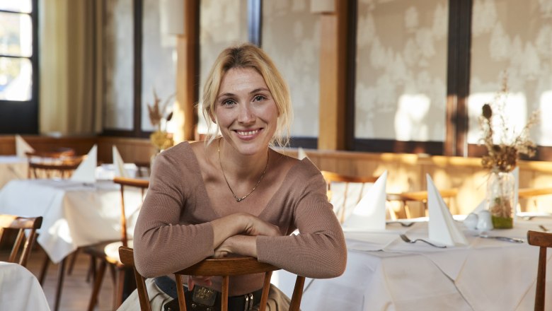 Katharina Bruckberger, © Niederösterreich Werbung/Andreas Hofer Woman sitting smiling in a restaurant with set tables.