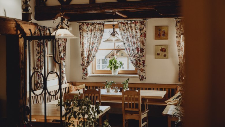 Hereinspaziert in die gute Stube, © Niederösterreich Werbung/Sophie Menegaldo Gemütlicher Raum mit Holzmöbeln, Pflanzen und geblümten Vorhängen.