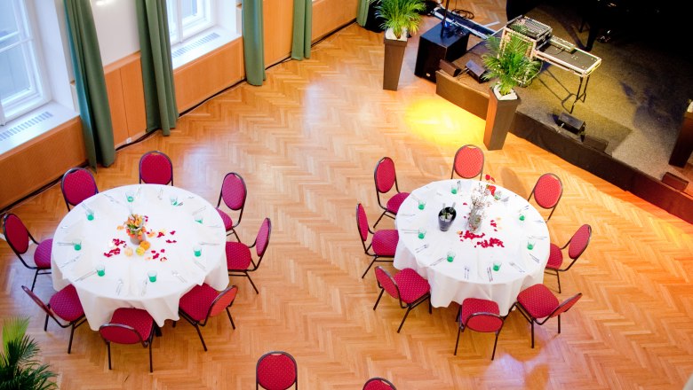 Hall, © dieStadtgalerie A festively decorated hall with round tables and red chairs, view from above.