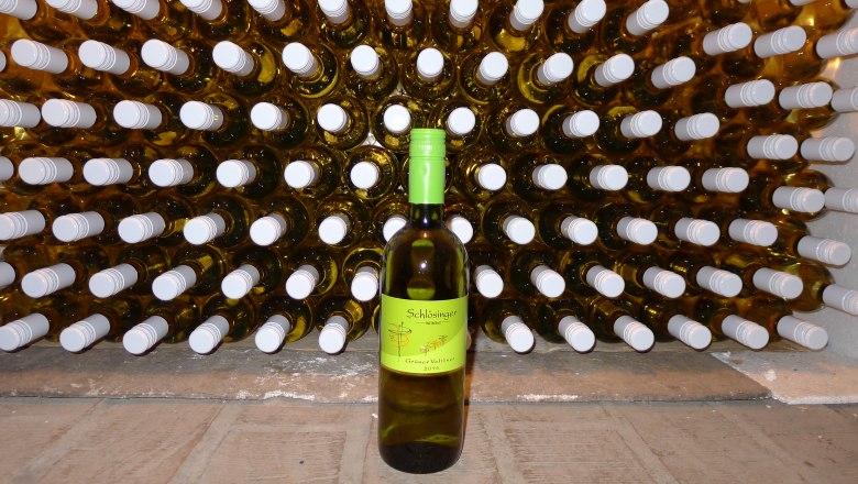 Wein, © Maria Schlösinger Eine Flasche Grüner Veltliner vor einem Regal voller Weinflaschen.