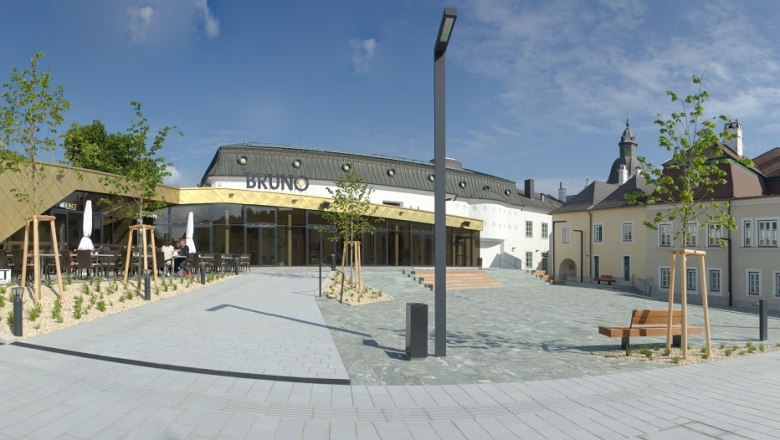 BRUNO, © Prinz Wolfgang Photography Moderne Architektur mit goldener Fassade und traditionellem Gebäude im Hintergrund, blauer Himmel.