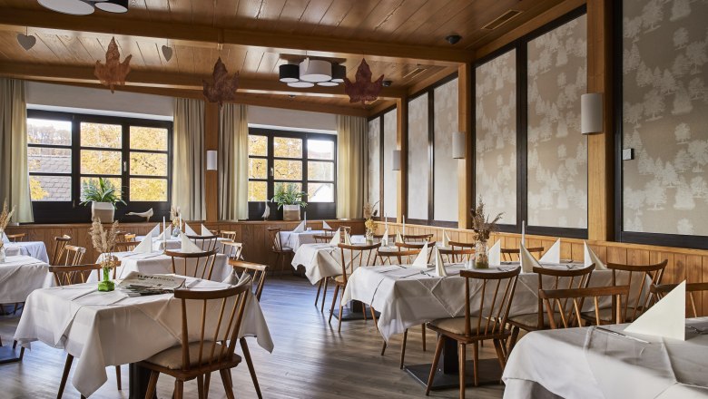 Bright, timeless ambience, © Niederösterreich Werbung/Andreas Hofer An elegant restaurant with wooden furniture, white tablecloths and large windows showing autumnal trees.
