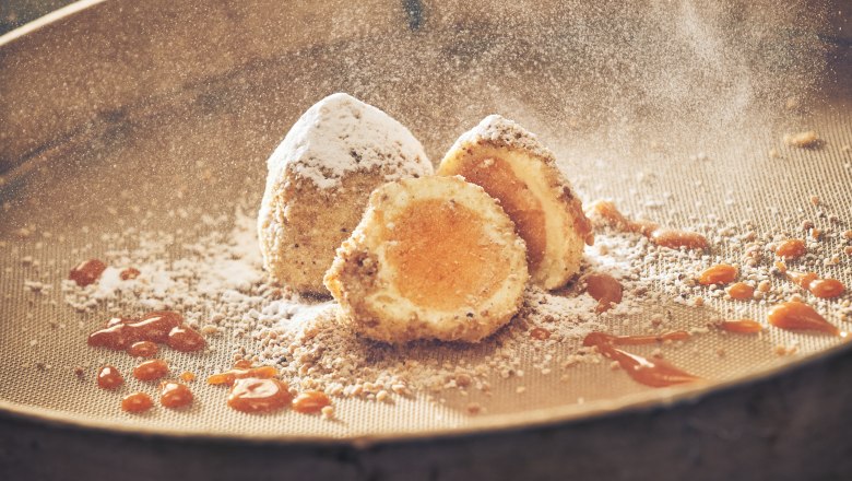 Eismarillenknödel, © Niederösterreich Werbung/Andreas Hofer Eismarillenknödel mit Puderzucker und Aprikosensauce auf einem Sieb.