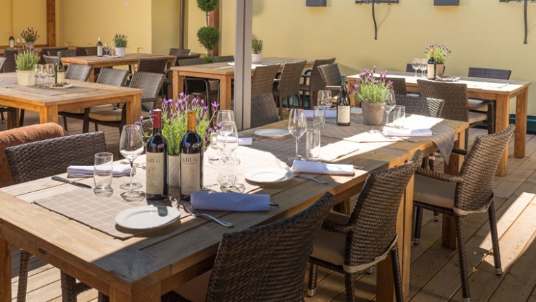 Terrasse Altes Zechhaus, © Wastian Eine Terrasse mit Holztischen, gedeckt mit Weinflaschen, Gläsern und Lavendel in Töpfen.