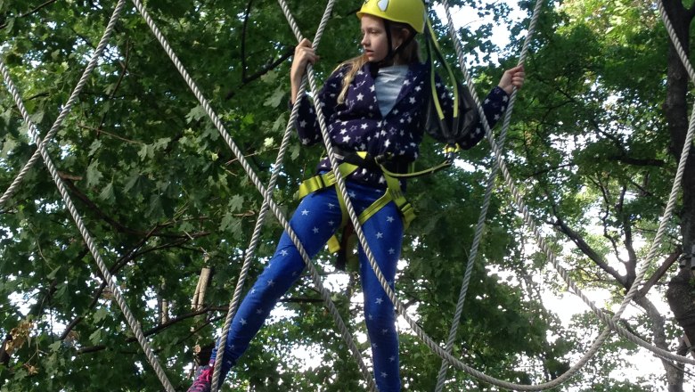 High ropes climbing in Tattendorf, © Soulriders/MB Child climbing high ropes in a climbing park surrounded by trees.