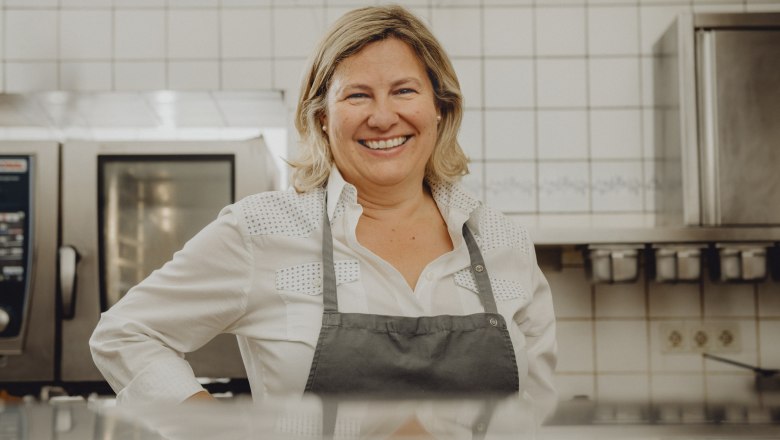 Landlady Claudia Schilling, © Niederösterreich Werbung/Rita Newman A smiling woman in a kitchen wearing an apron.