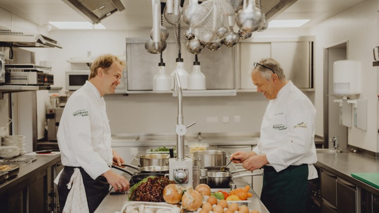 Cooking together Rainer & Robert Schüller, © Niederösterreich Werbung/Rita Newman Two chefs in a professional kitchen cooking together. There are vegetables and eggs on the table.