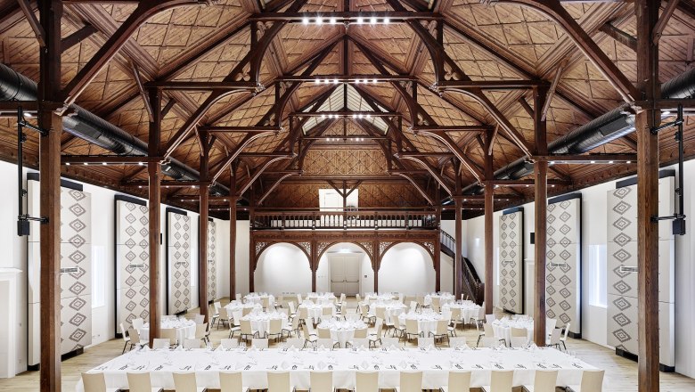 GABRIUM ballroom, © amm - architektin mautner markhof Interior view of a large banqueting hall with wooden beamed ceiling and covered tables.