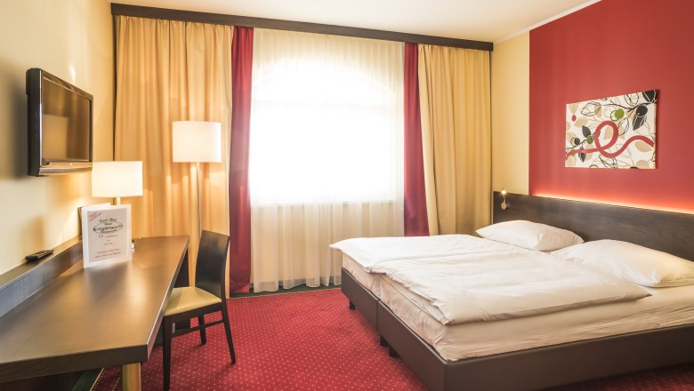 Hotelzimmer, © hotelkarlwirt Ein gemütliches Hotelzimmer mit Doppelbett, rotem Teppich, Schreibtisch, Fernseher und moderner Kunst an der Wand.