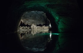 Blauer See, © Seegrotte Dunkle Höhle mit Wasser und Felsformationen, beleuchtet von grünlichem Licht.