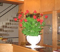 Innen, © Rosner Ein Blumenarrangement mit roten Rosen in einer weißen Vase auf einem Tisch in einem Innenraum.