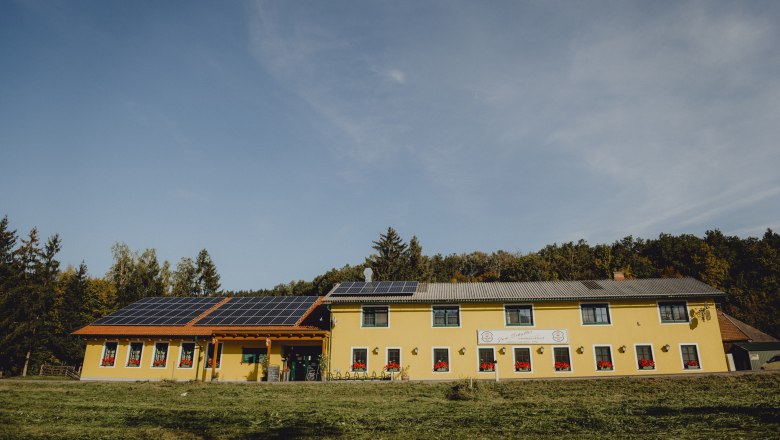 Landgasthof mit Microhotels, © Niederösterreich Werbung/Rita Newman Gelbes Gebäude mit Solarpanelen auf dem Dach, umgeben von Bäumen.