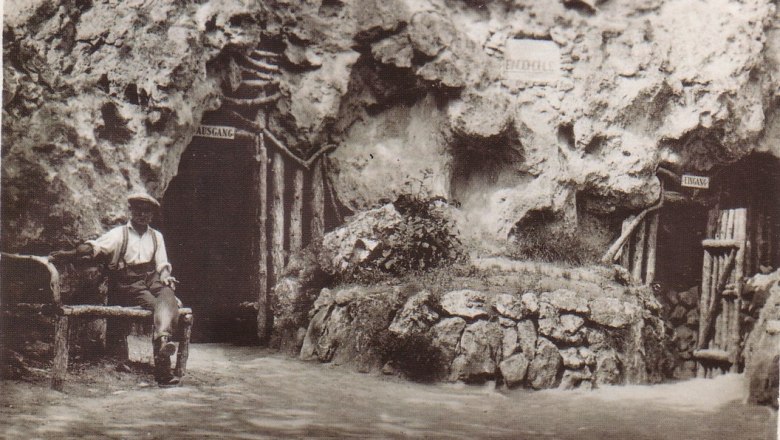 Einödhöhle, © Marktgemeinde Pfaffstätten Historisches Foto der Einödhöhle in Pfaffstätten, Baden, mit einem Mann auf einer Bank vor dem Höhleneingang.