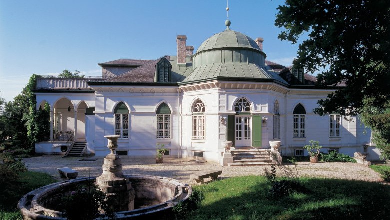 Geymüllerschlössel, © MAK/Wolfgang Kraus Das Geymüllerschlössel, ein historisches Gebäude mit Kuppeldach und Rundbogenfenstern, umgeben von Bäumen und einem Brunnen im Vordergrund.