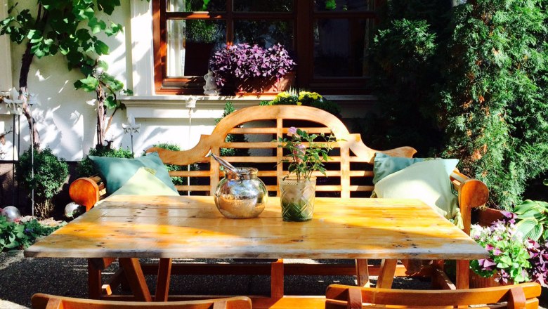Wine tavern Schwertführer, © Schwertführer Cozy garden area with wooden table and chairs, surrounded by plants and vines.