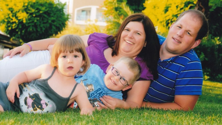 Familie, © Maria Schlösinger Eine Familie liegt lächelnd auf einer Wiese, bestehend aus zwei Erwachsenen und zwei Kindern.