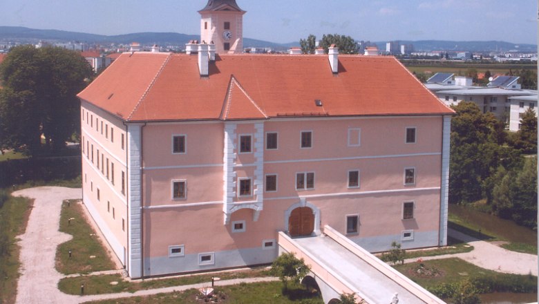 Vösendorf Castle with red roof and clock tower, surrounded by green spaces.