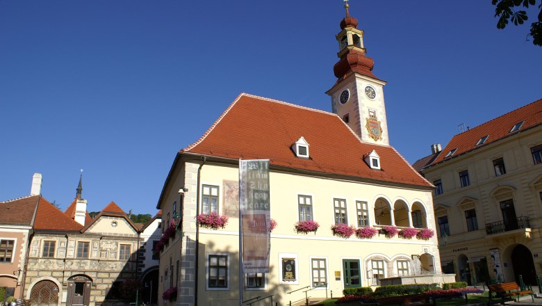 Historisches Gebäude mit Turm und Uhr in Mödling, umgeben von blauen Himmel.