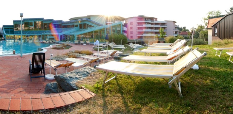 A pool area with sun loungers and a modern building in the background.