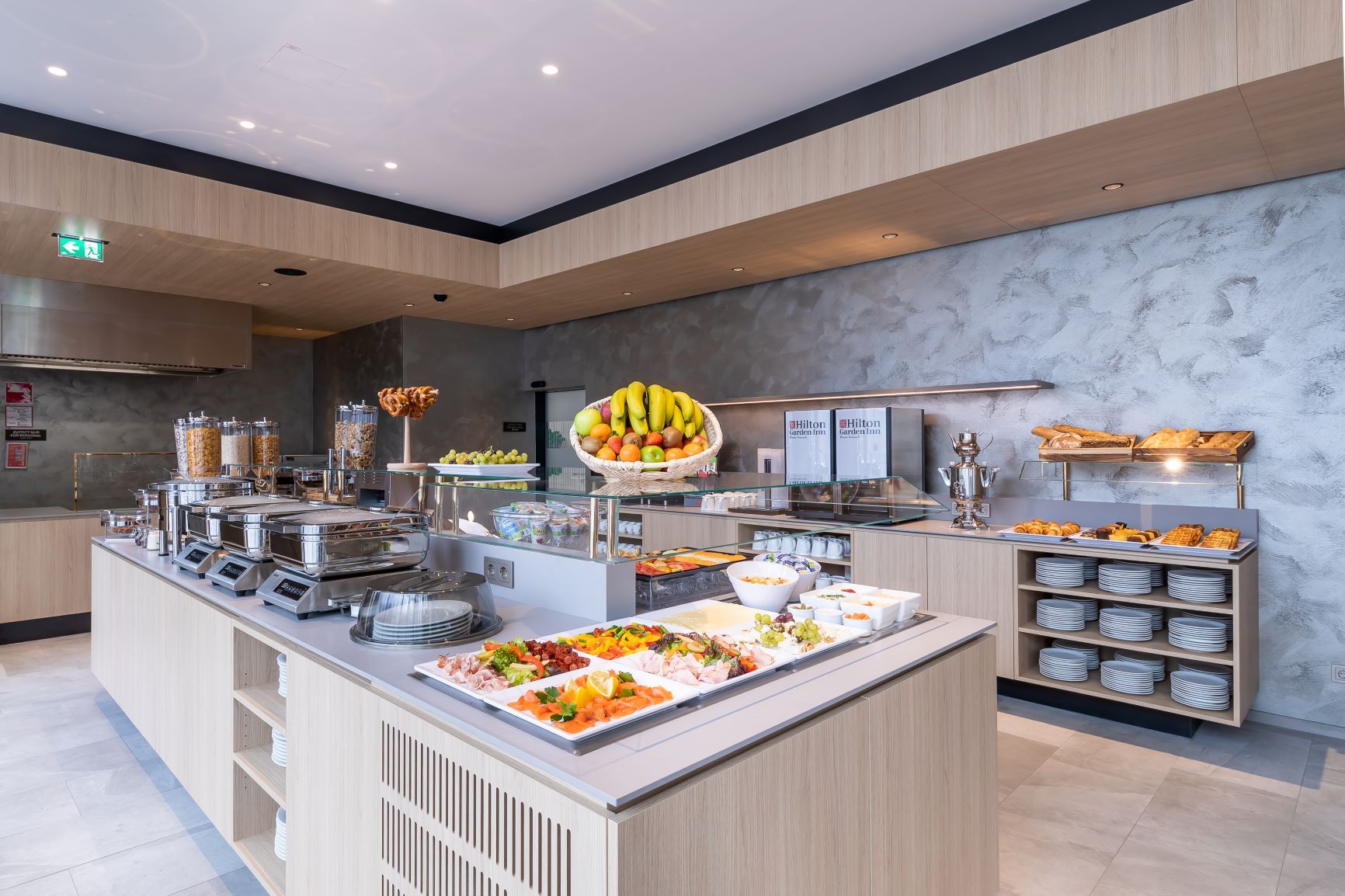 Ein reichhaltiges Frühstücksbuffet mit Obst, Gebäck, Aufschnitt und Cerealien in einem modernen Hotelrestaurant.