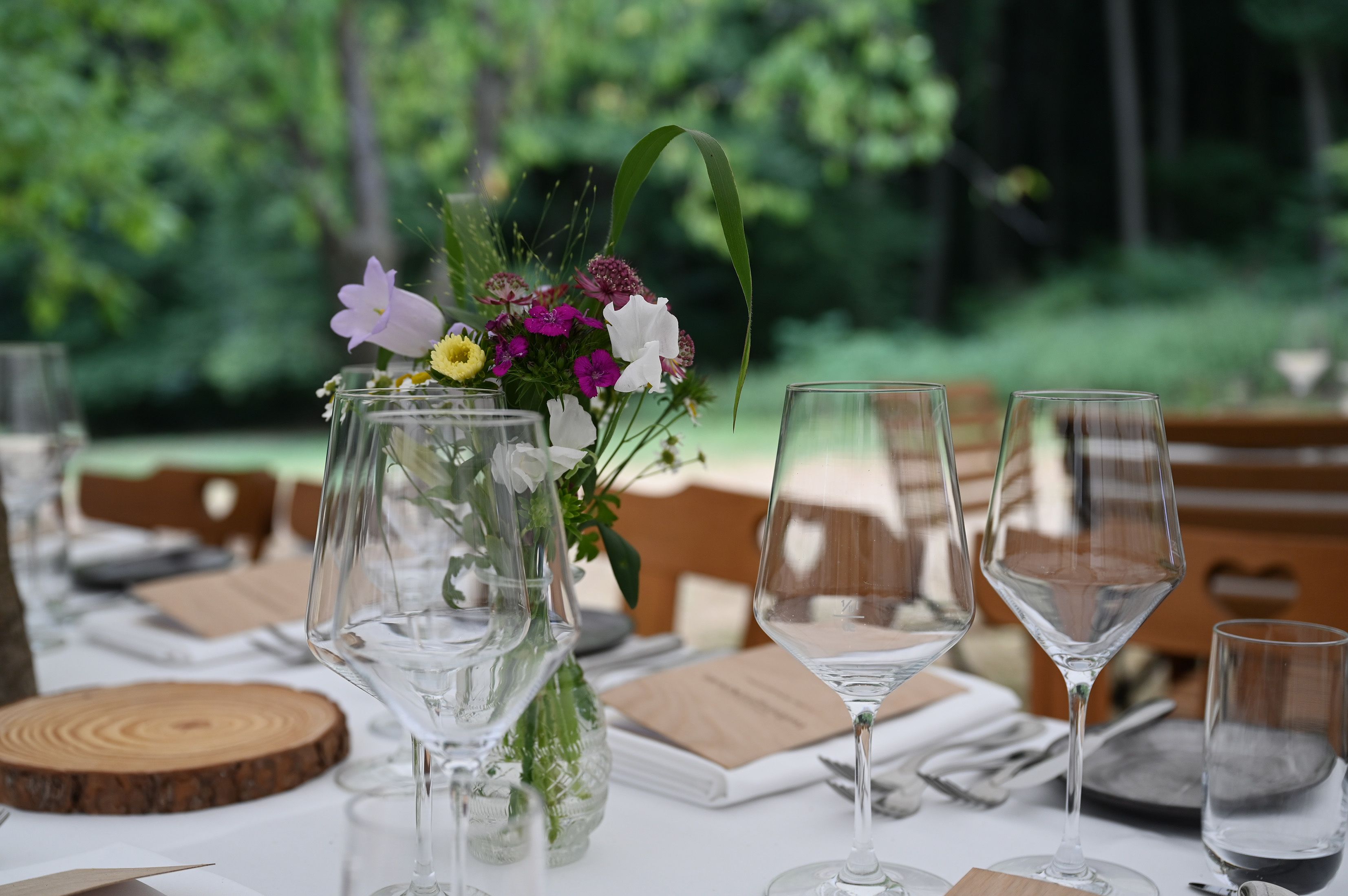 Schön gedeckter Tisch am Waldrand, darauf zu sehen ist ein weißes Tischtuch und frischer Blumenschmuck.