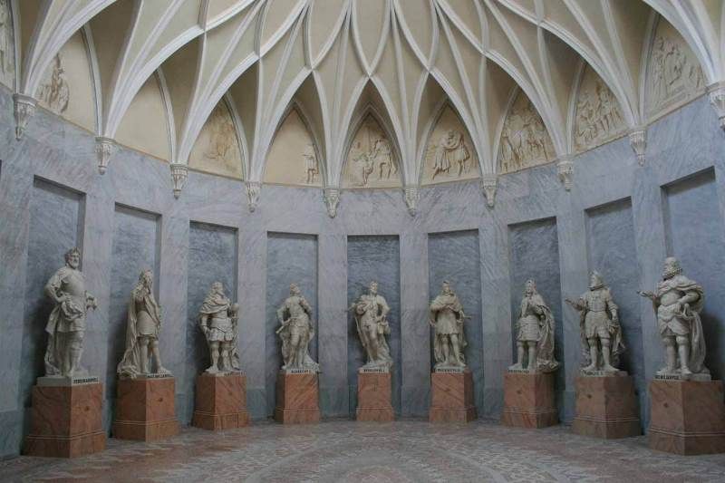 Innenansicht des Habsburgersaals mit Statuen auf Sockeln und einem gewölbten Deckenmuster.