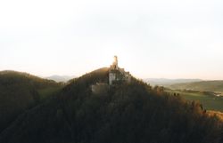 Die sanften Hügel umarmen die majestätische Ruine, während die goldenen Strahlen der Abendsonne die Landschaft in ein warmes Licht tauchen. Hier, wo die Natur und Geschichte aufeinandertreffen, lädt die atemberaubende Aussicht dazu ein, die Seele baumeln zu lassen und die Stille der Umgebung zu genießen.