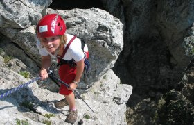 Person klettert an Felsen mit rotem Helm und Seil.